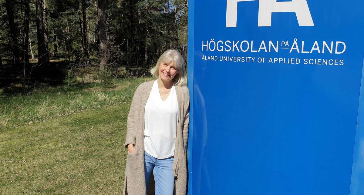 Bettina lutar sig mot skylt med texten Högskolan på Åland.